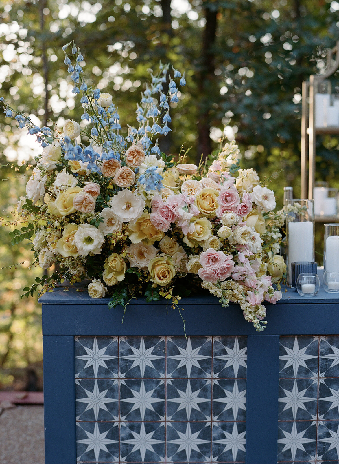 Lush flower forward bar statement arrangement with emphasis on yellow florals and touches of pink and blue. Cosmic wedding rehearsal theme at observatory with pastel florals and moody blues. Tented wedding rehearsal dinner with lush fall florals such as dahlias, garden roses, and lisianthus. Design by Rosemary & Finch Floral Design in Nashville, TN.