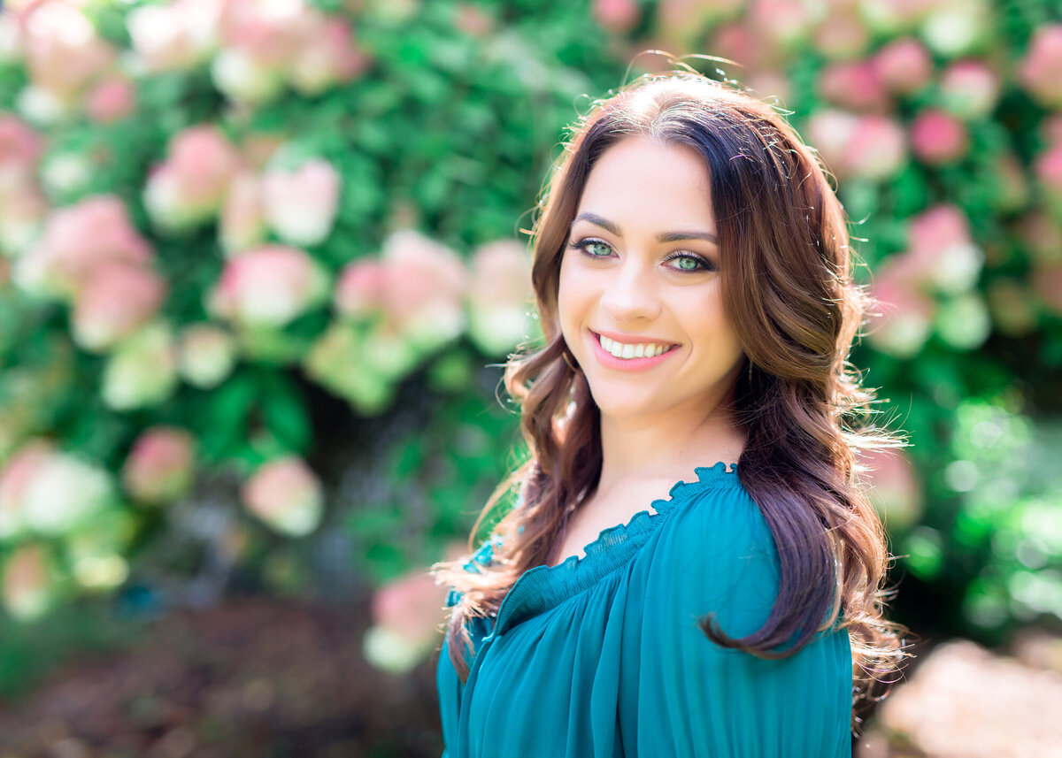 Female headshot client standing outside in front of a flowering bush