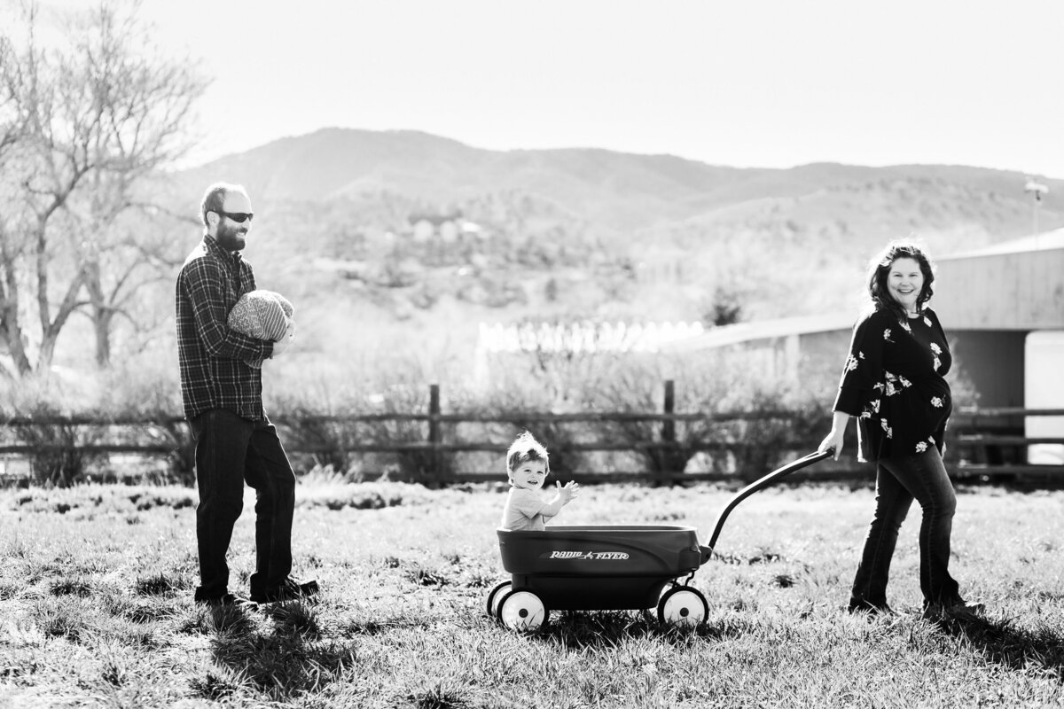 a mom pulls son in wagon while dad carries newborn