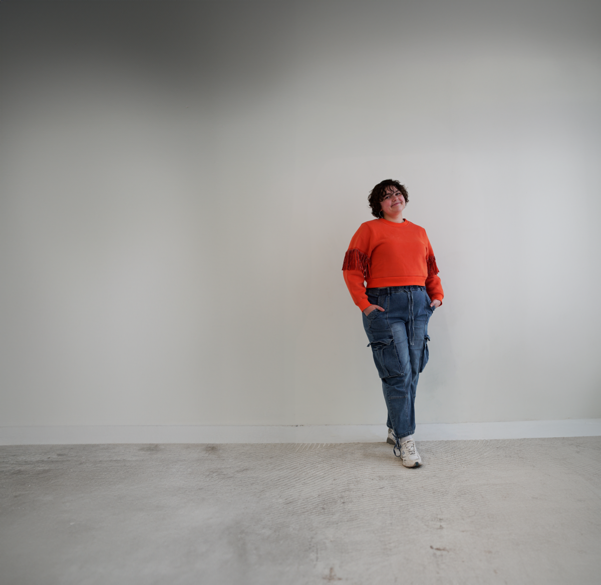 woman with short brown curly hair standing with orange sweater and blue jeans - toronto-based luxury brand designer for beauty industry