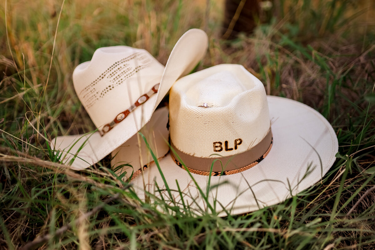Close-up of monogrammed cowboy hat with engagement ring placed on top during Harper Hills engagement session in New Braunfels, Texas.