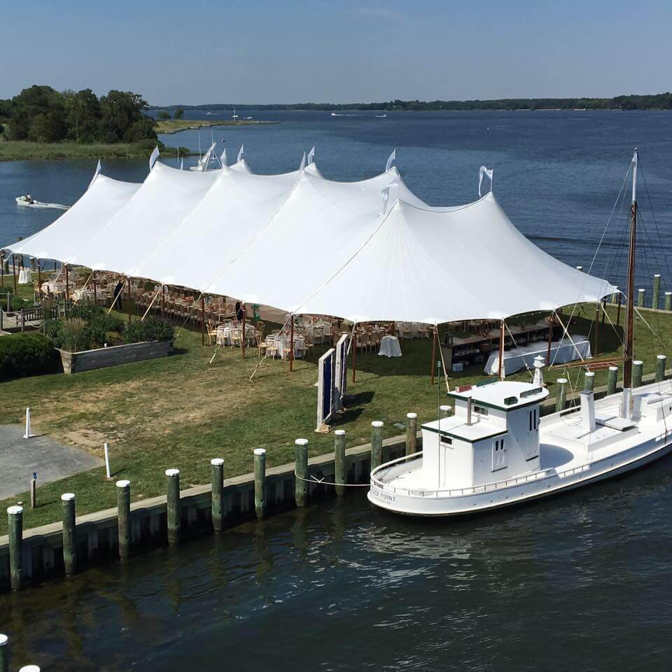 A stunning double pole marquee set up on the edge of the water with a boat docked next to it.