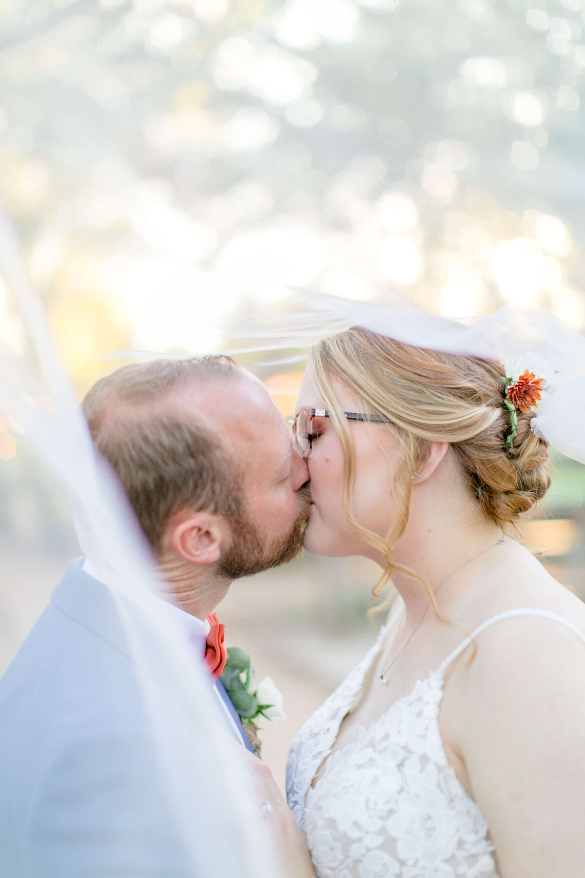 groom in bright blue suit kissing his red headed bride underneath her vail.