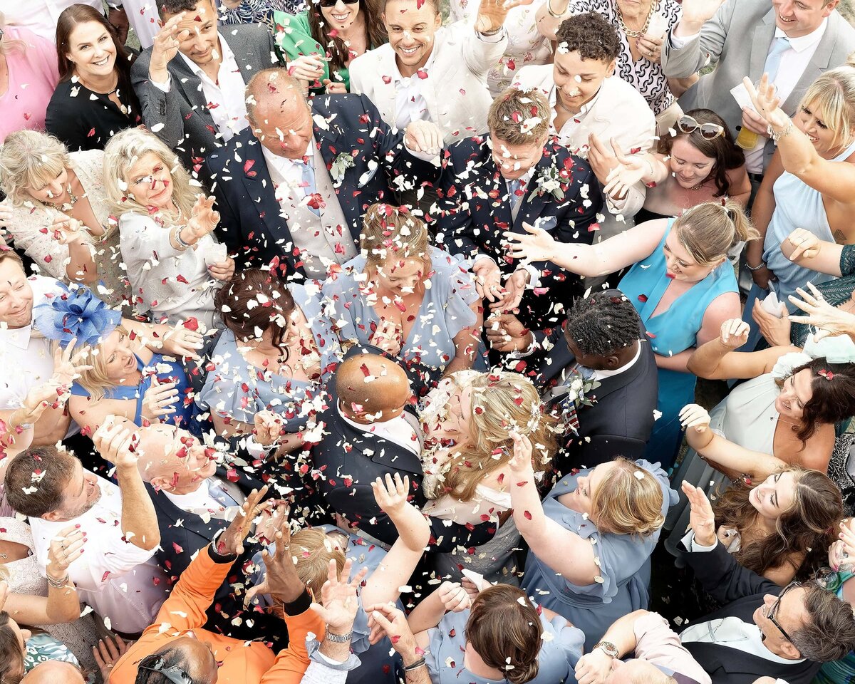 Bride and groom embracing surrounded by their guests while having confetti thrown at them seen from above.