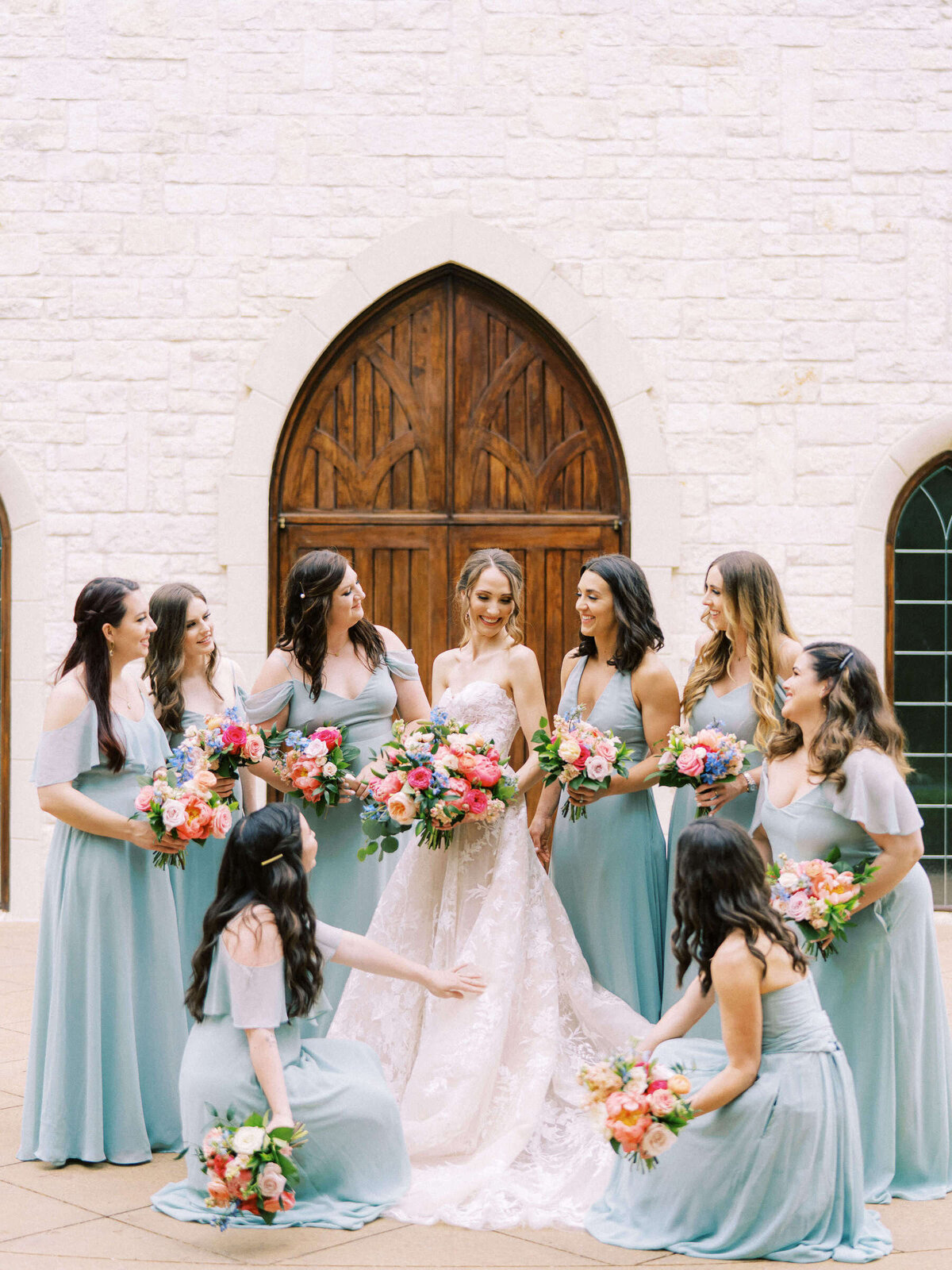 Bridesmaids in aqua dresses help fix bride's Monique Lhuillier wedding dress outside Ashton Gardens wedding chapel