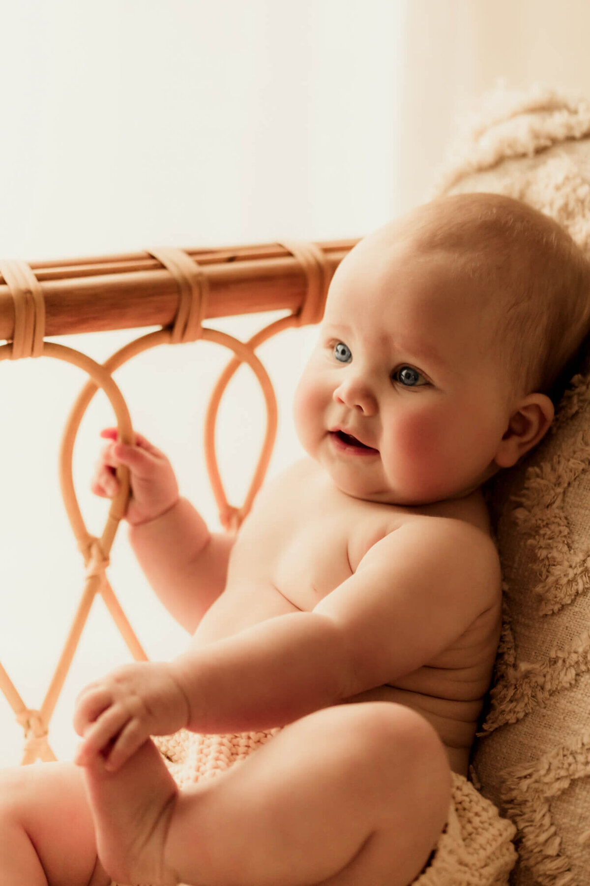 Baby girl holding her toes with  her hand placed on a rattan daybed.