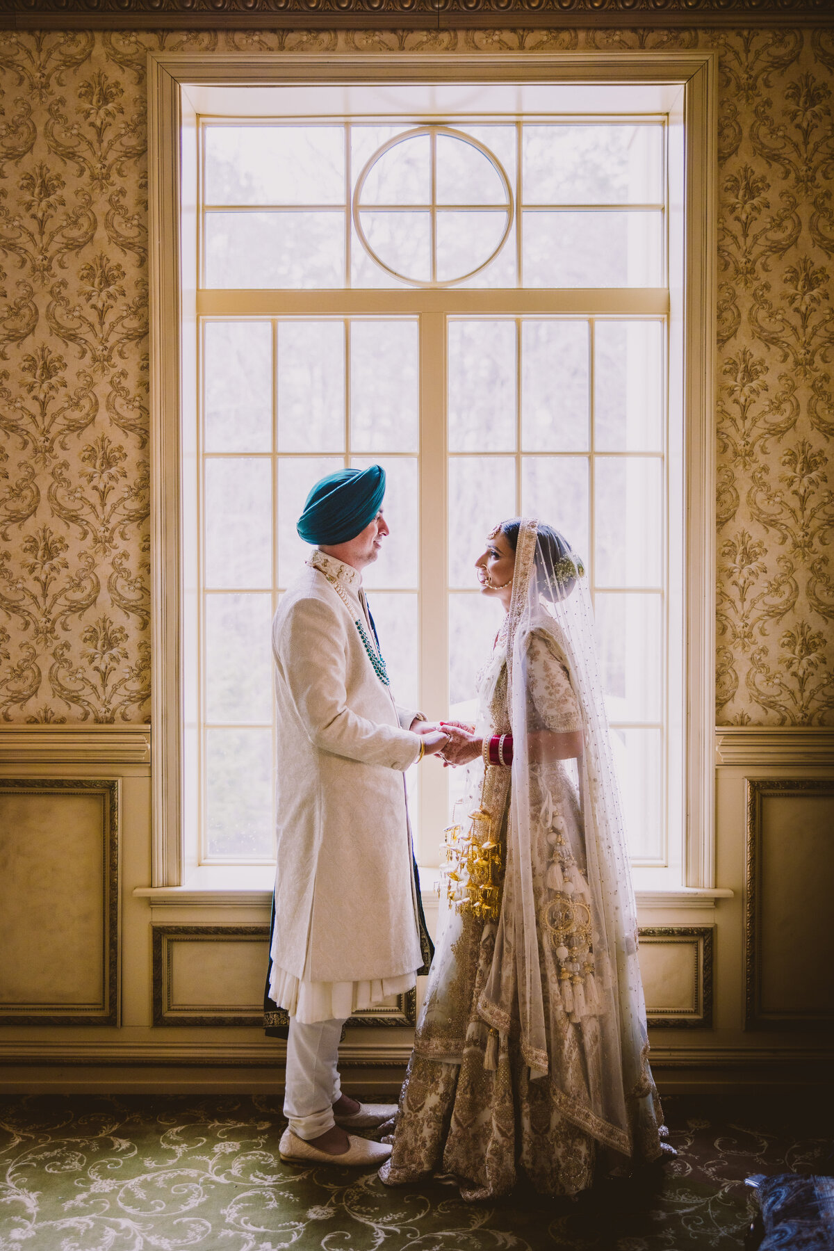 A sikh bride and groom holding hands and looking at each other in front of a window at Brigalias NJ