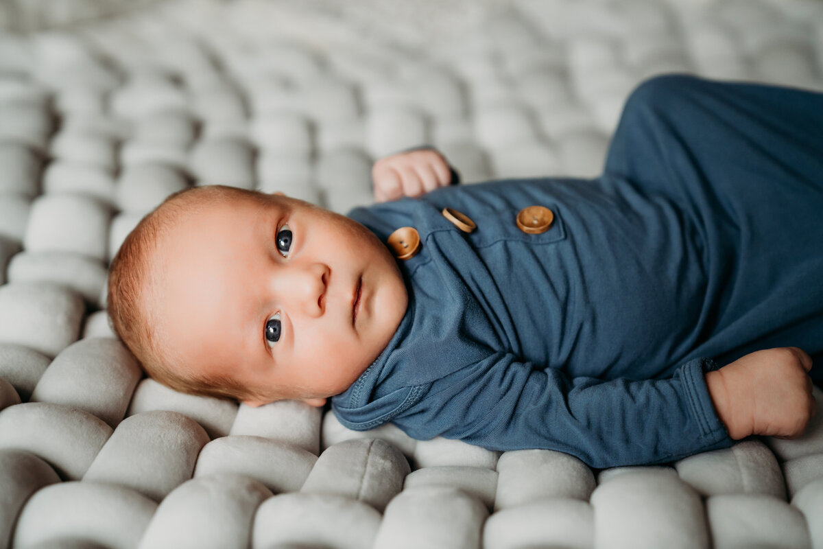 Newborn Photographer, a baby boy lays on bed covers with eyes wide open and alert