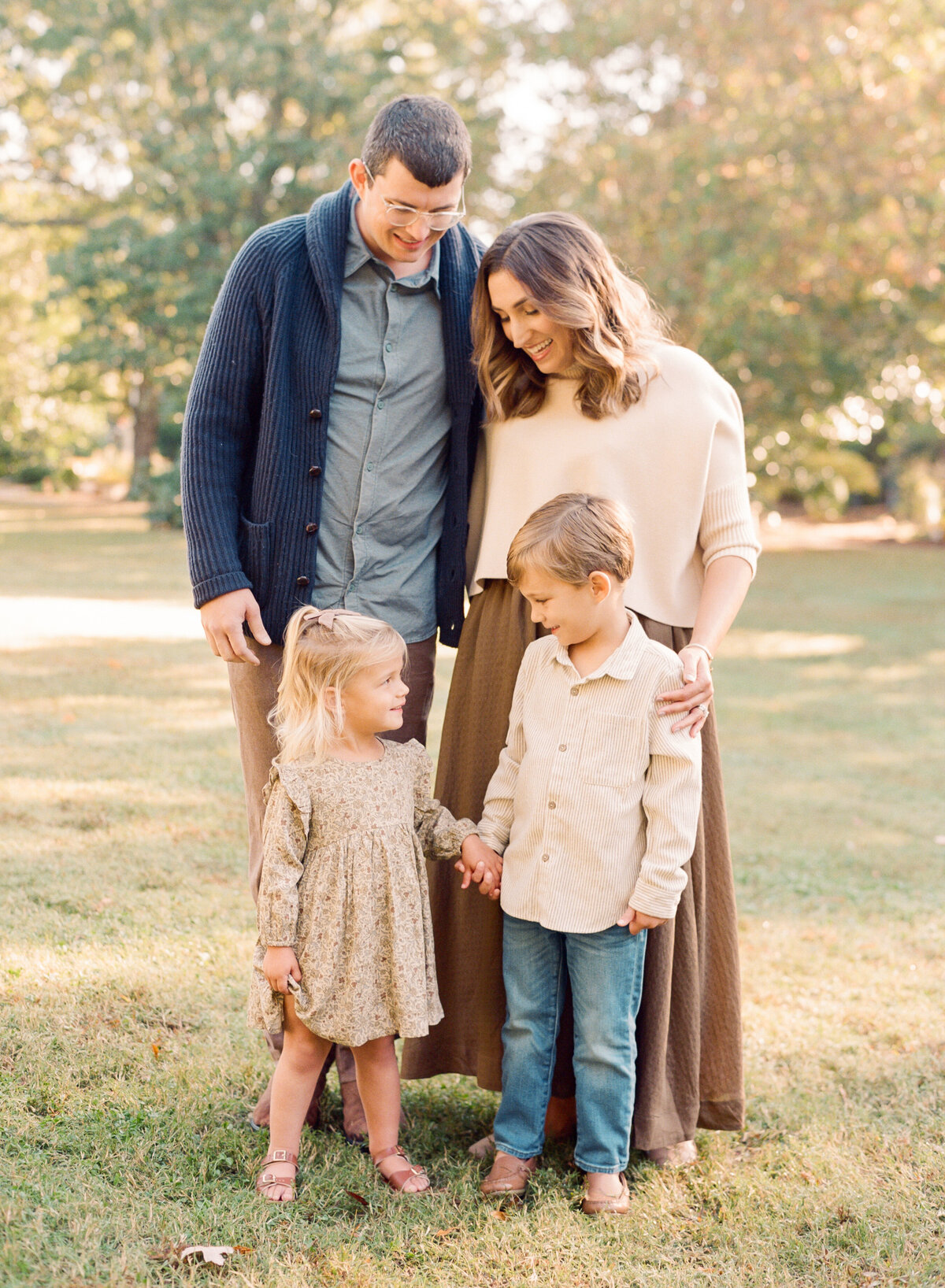 family holds hands and smiles at each other during their family session in wake forest nc. Family walking during their family portrait session in Wake Forest, NC. Photographed by Raleigh family photographer A.J. Dunlap Photography.