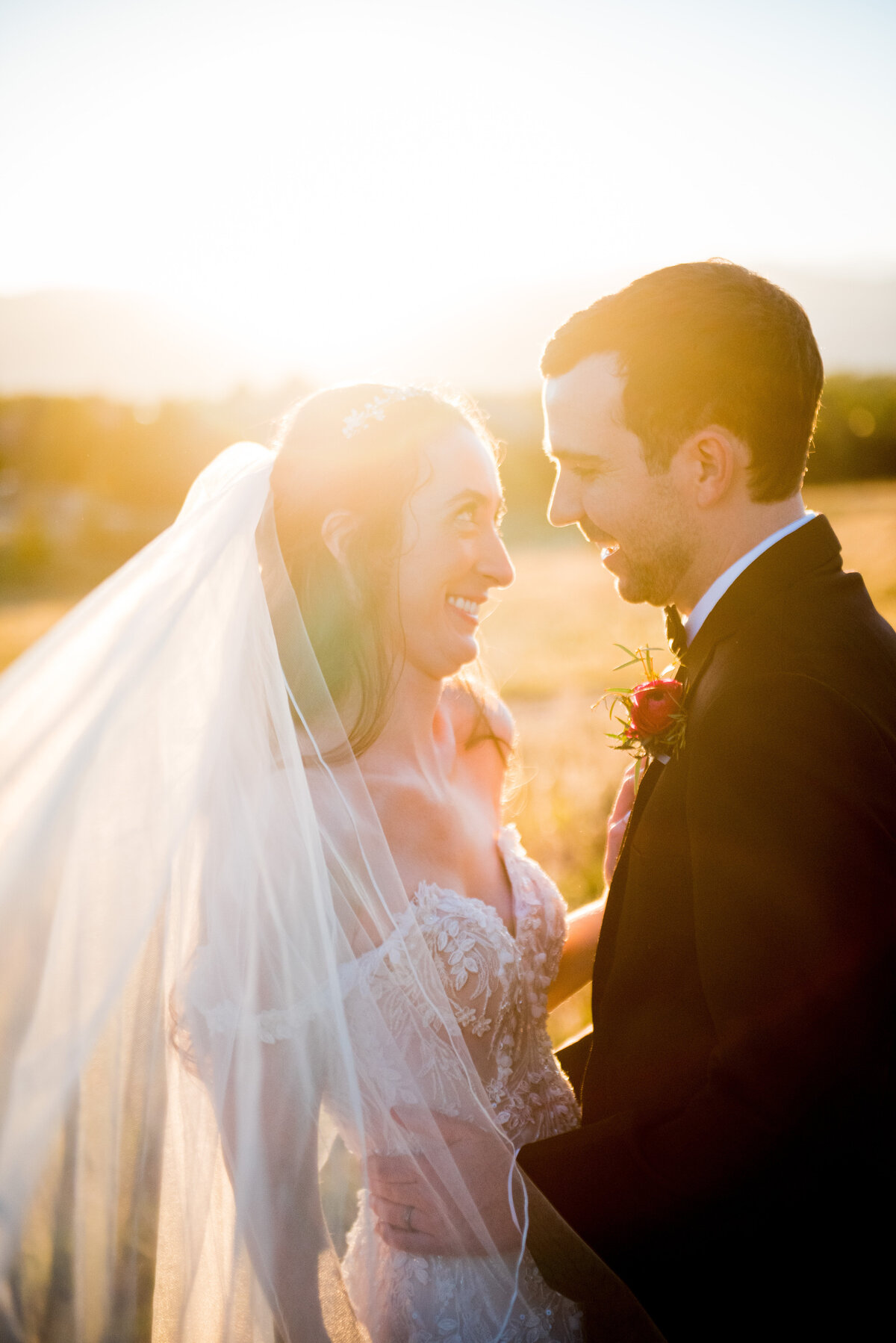 A bride and groom smile at each other as the sun sets behind them during golden hour, captured by Denver wedding photographer, Two One Photography.
