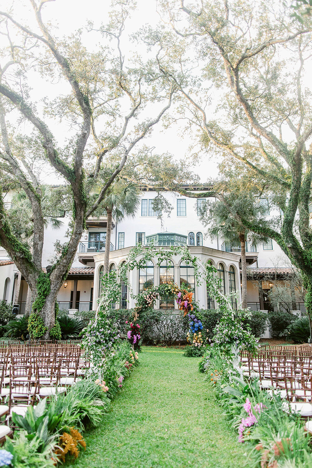 Ceremony space full of greens and flowers backdropped by a large mansion.