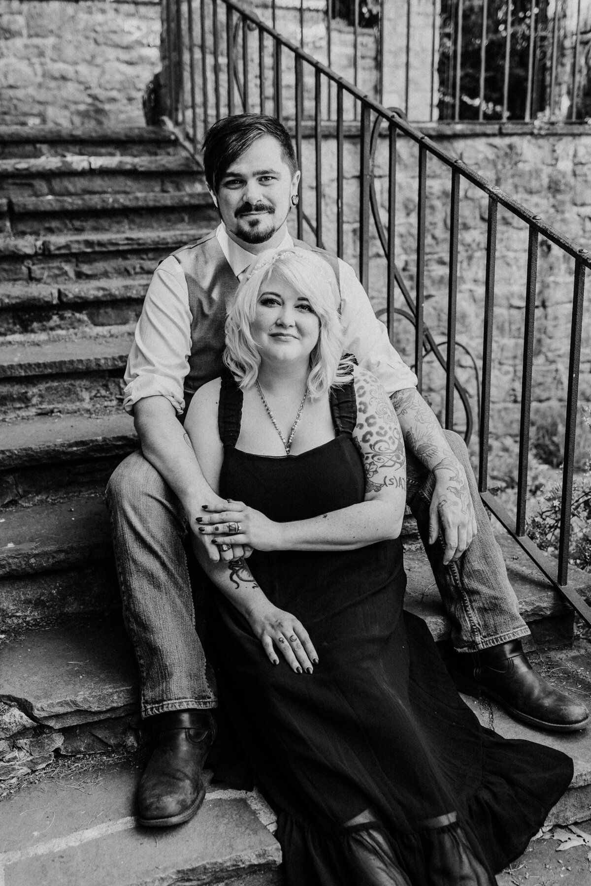 An engaged couple snuggles while sitting on stone garden stairs in black and white