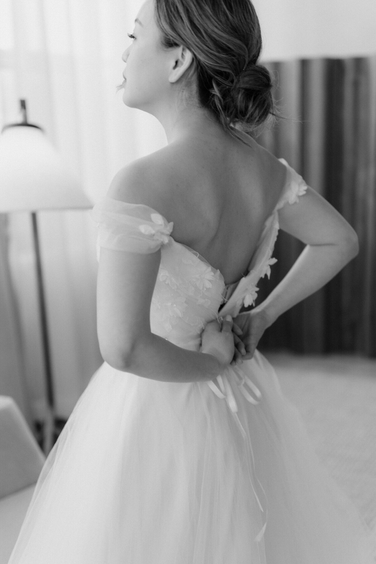 Bride trying to fix her dress while getting ready in a hotel.