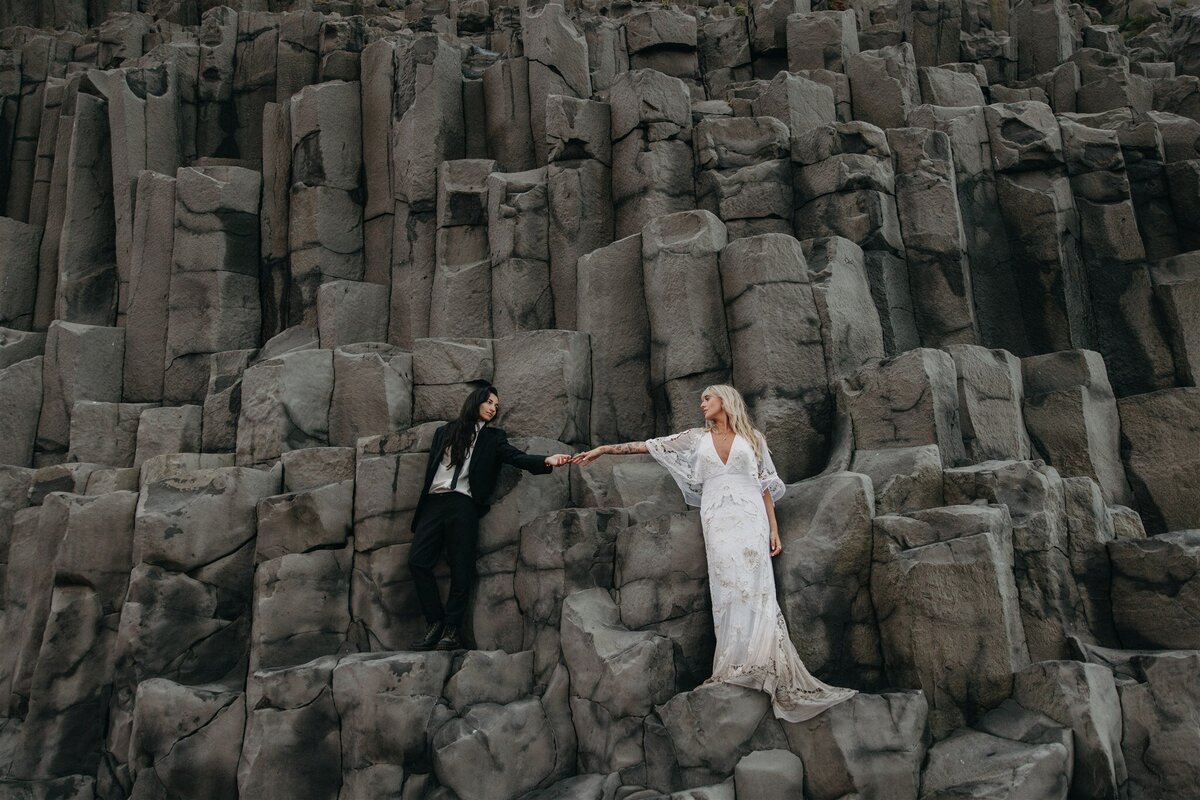 Eloping couple holding hands on dramatic basalt cliffs in Iceland, captured by a destination elopement photographer.