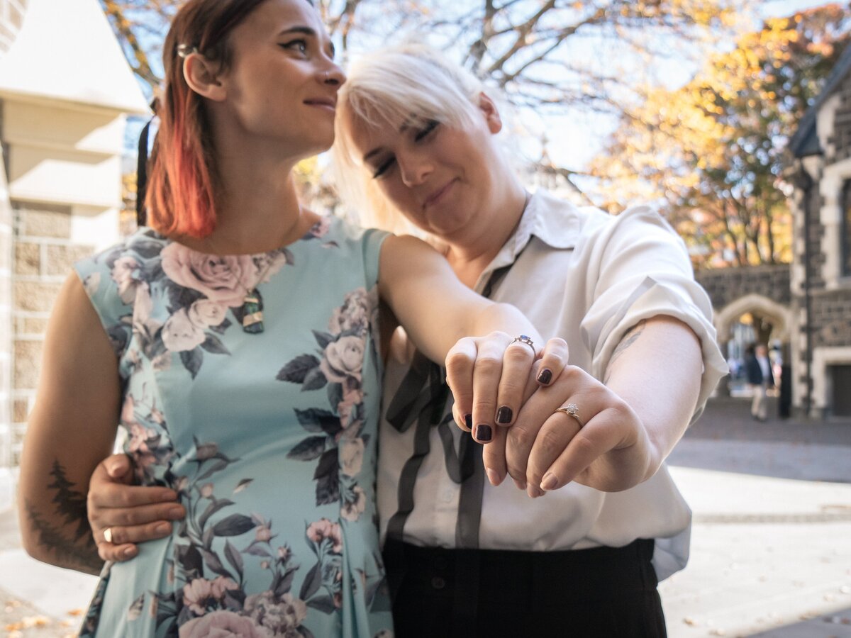 a queer couple show off their engagement rings with photos at Hagley Park in Christchurch, New Zealand.