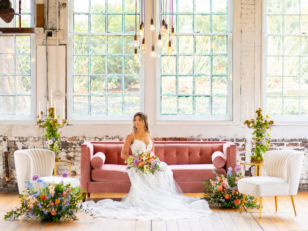 Bride sitting on pink velvet couch surrounded by flowers