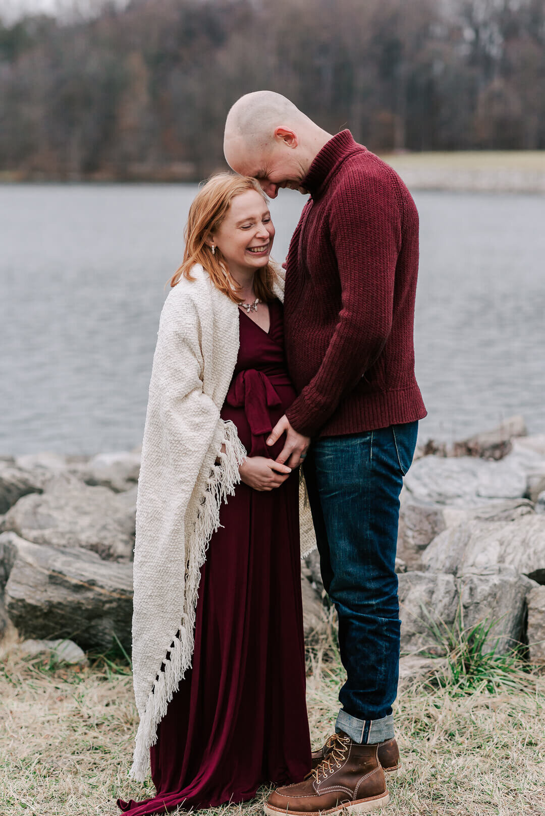 Expecting parents wearing burgundy tones giggling together during their session with northern virginia maternity photographer