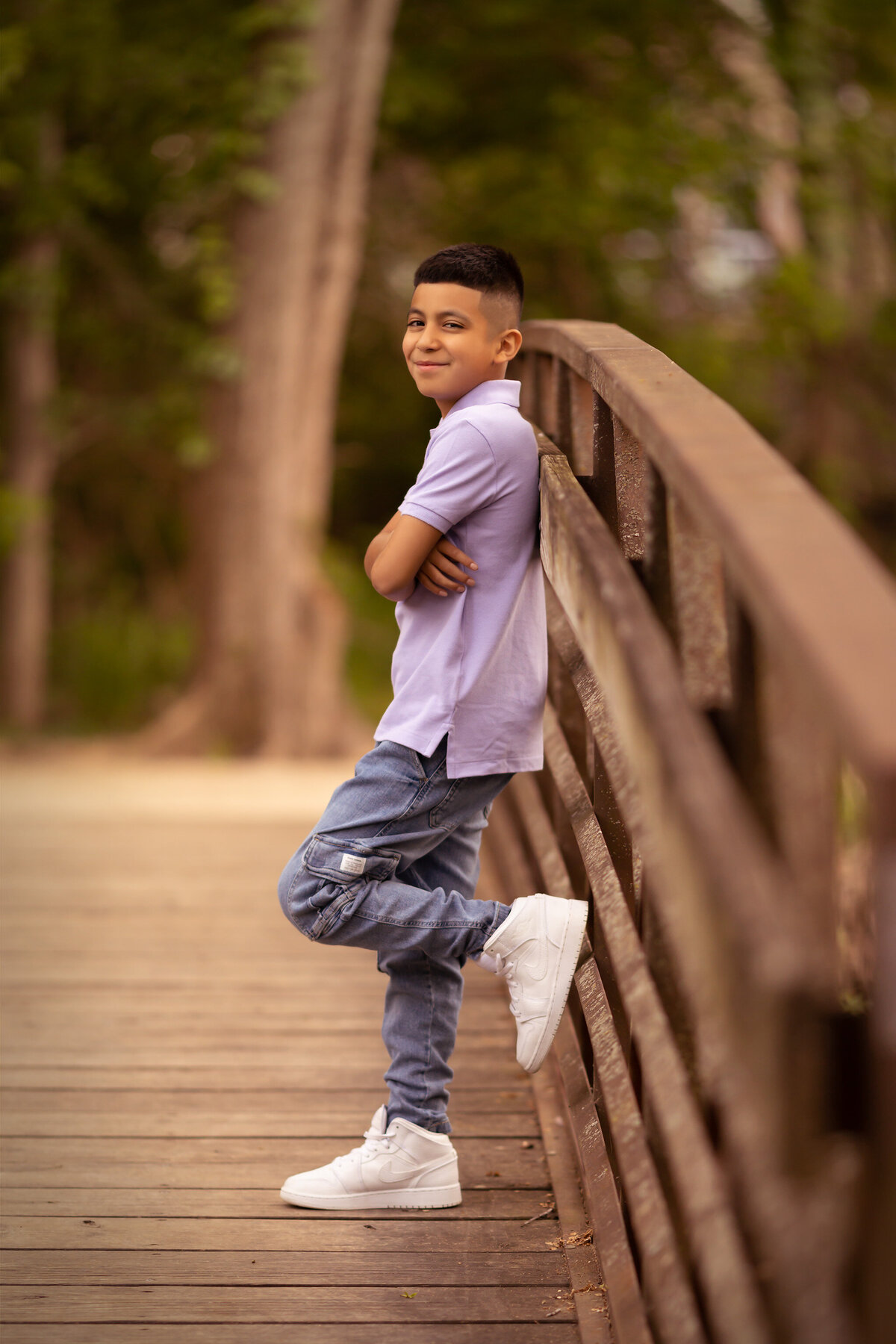 Family portraits in Dallas feature a young boy with a confident smile, leaning against a wooden bridge in casual attire.