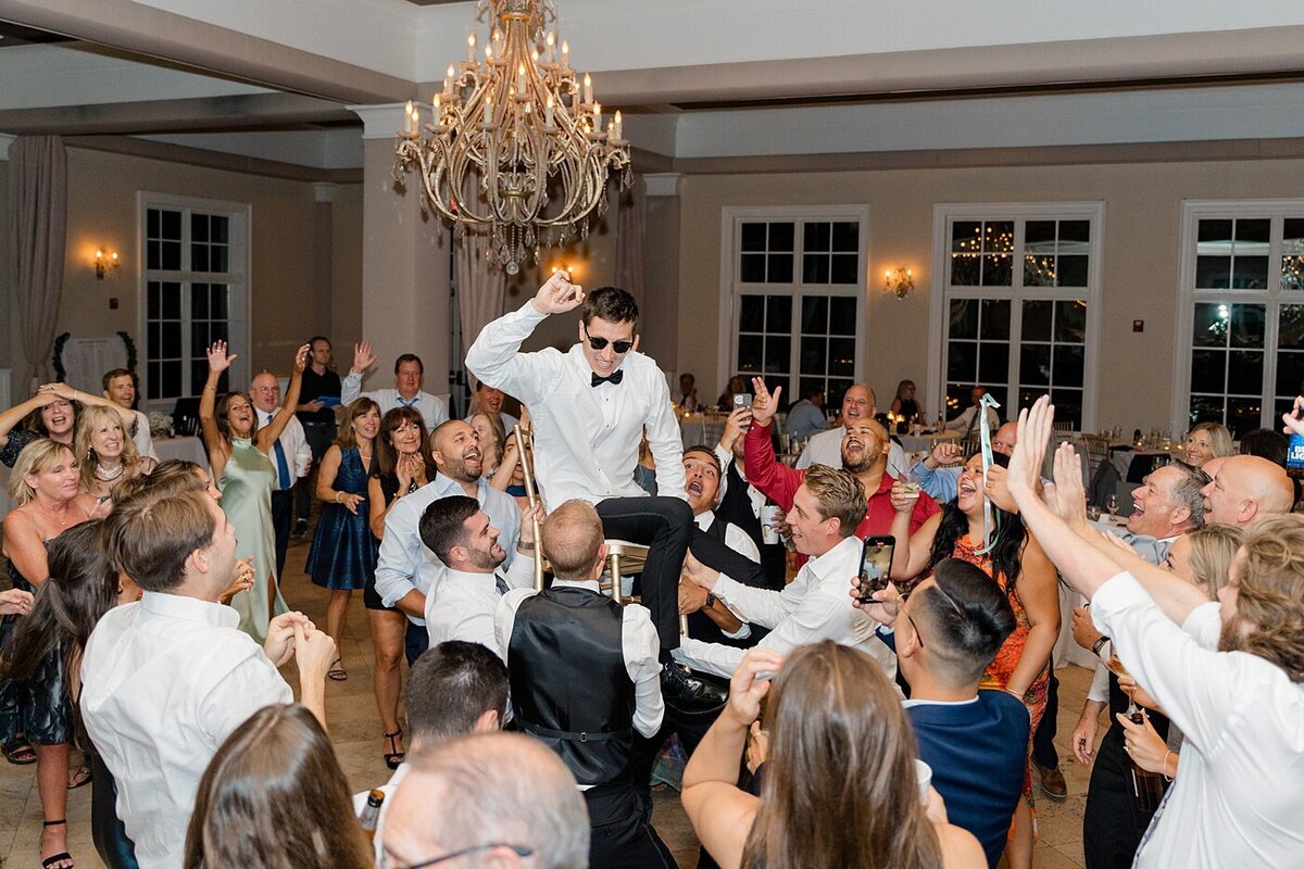 groom on a chair while his groomsmen raise the chair and the guests dacne around him during their reception at the Pinnacle
