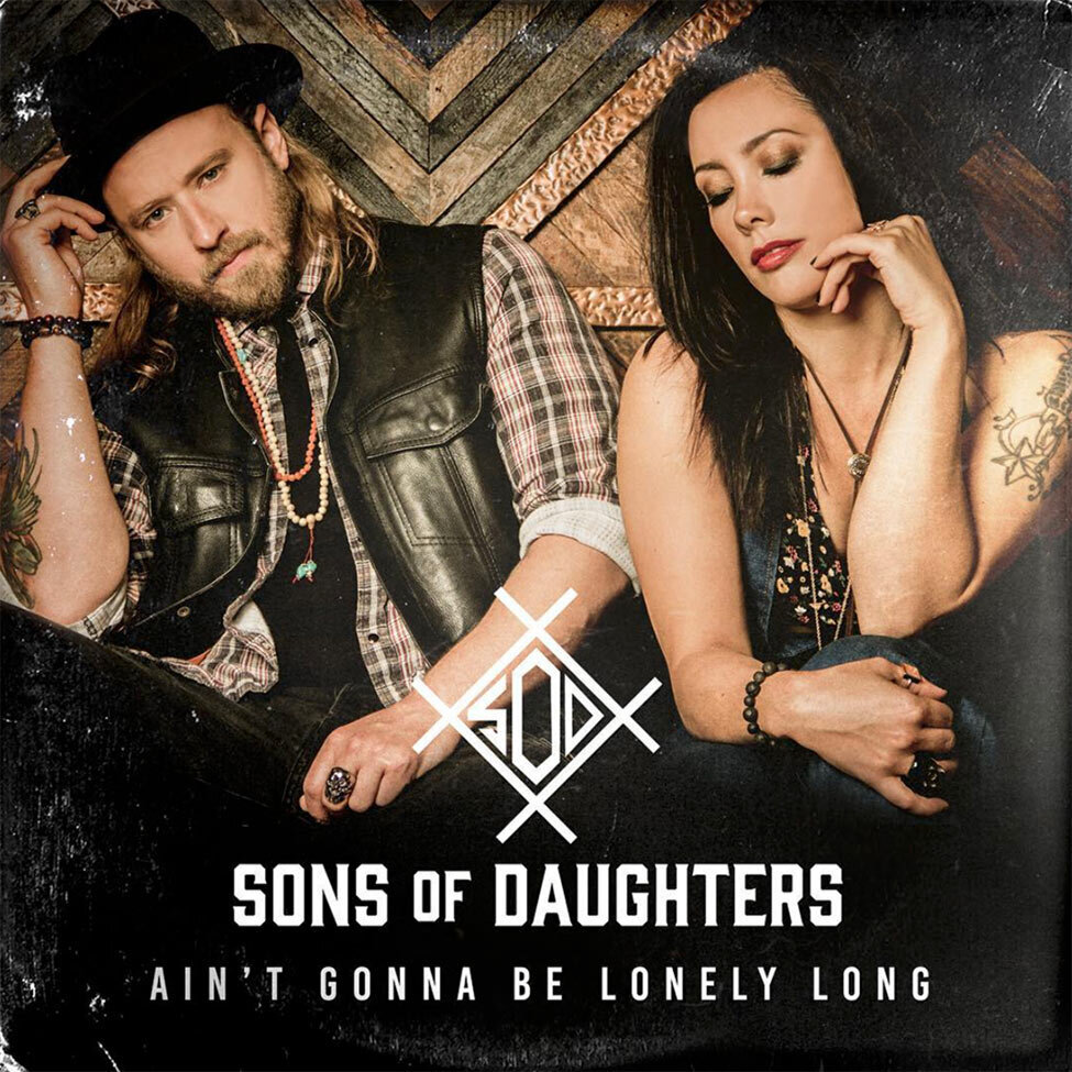 Nashville Single Cover Title Aint Gonna Be Lonely Long Artist Sons of Daughters dup sitting in front of wood wall with triangle pattern male band member looking at camera while tipping black hat female band member looking down hand to her chin