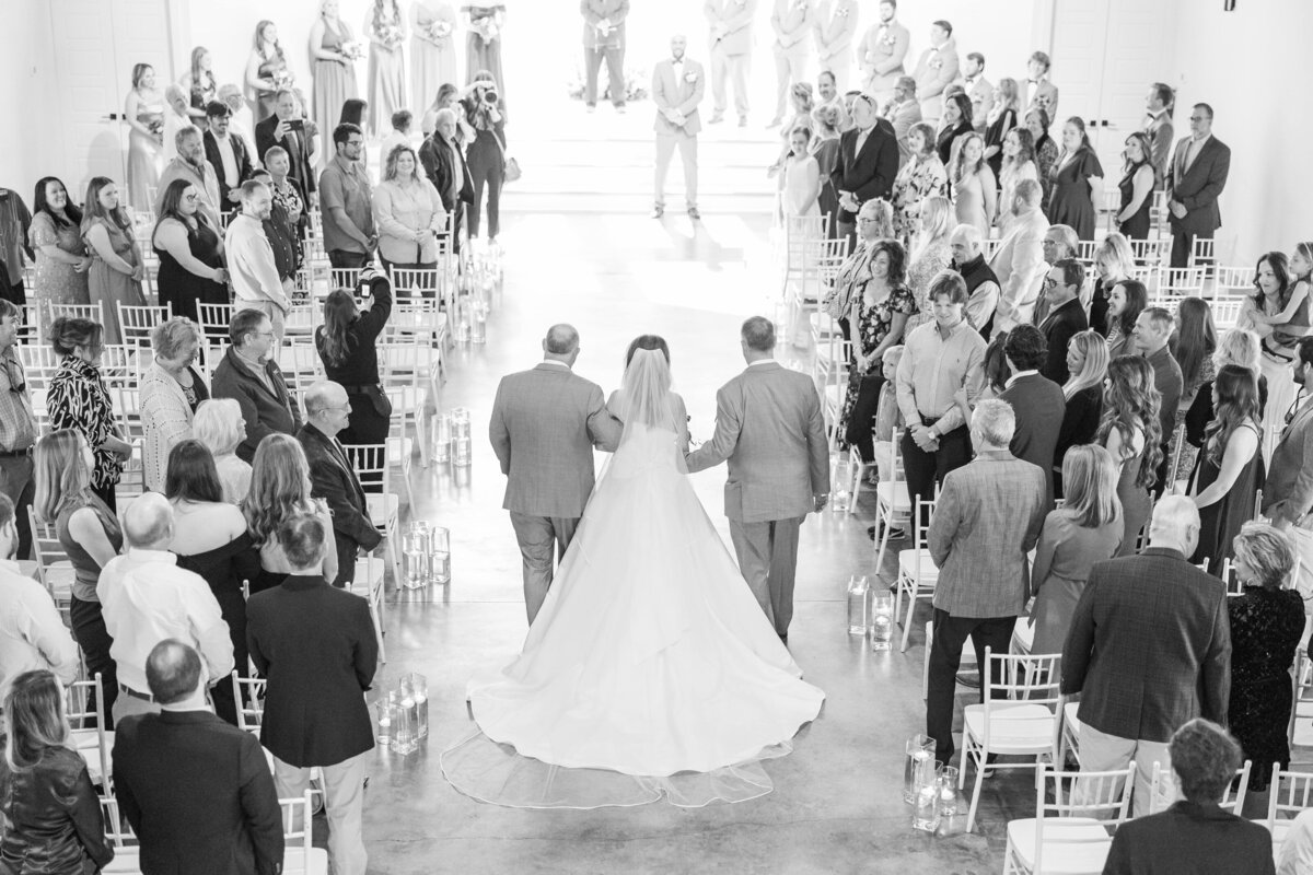 A bride walks down the aisle escorted by two men to the altar as seen from above by an Arkansas wedding photographer