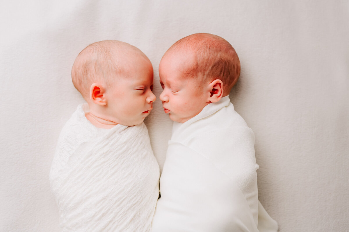 twin baby boy and baby girl gentaly wrapped up and facing each other, nose to nose