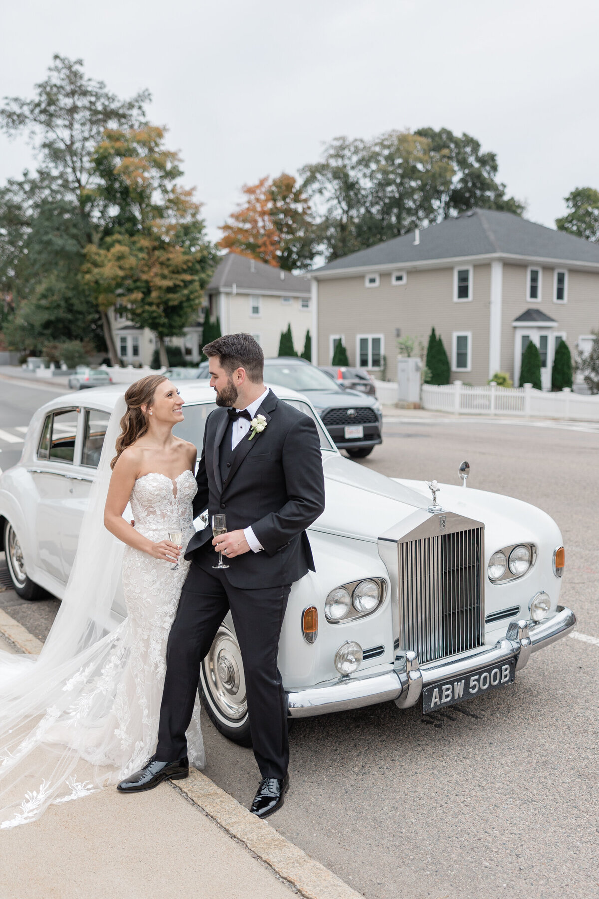 A bride and groom share a glass of champagne by a vintage Rolls Royce