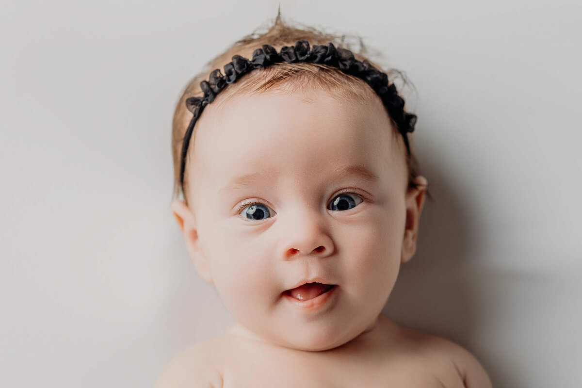 wide awake baby girl with a black headband on a white backdrop for older newborn photos in york 