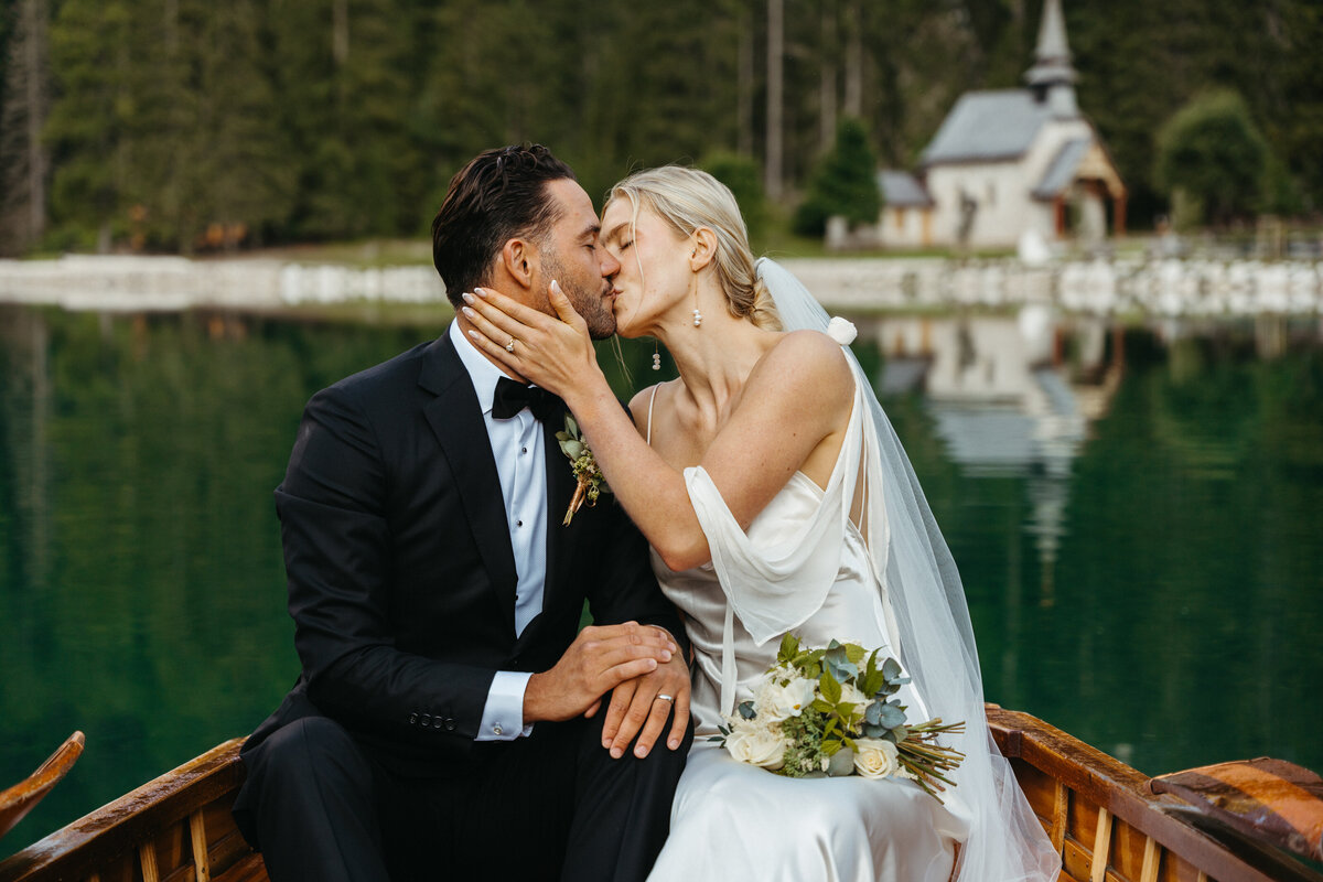 Bride and groom kissing while sitting in wooden boat on Lago di Braies