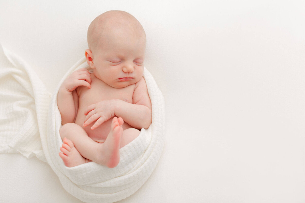 Baby wrapped in a white swaddle with arms and feet out sleeping during her newborn photoshoot in pdx.