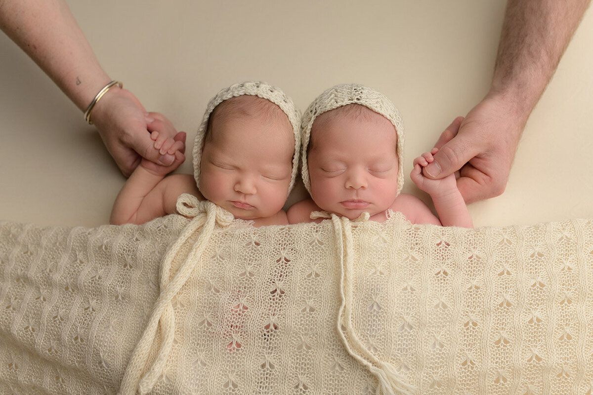 twin newborns holding parents hands