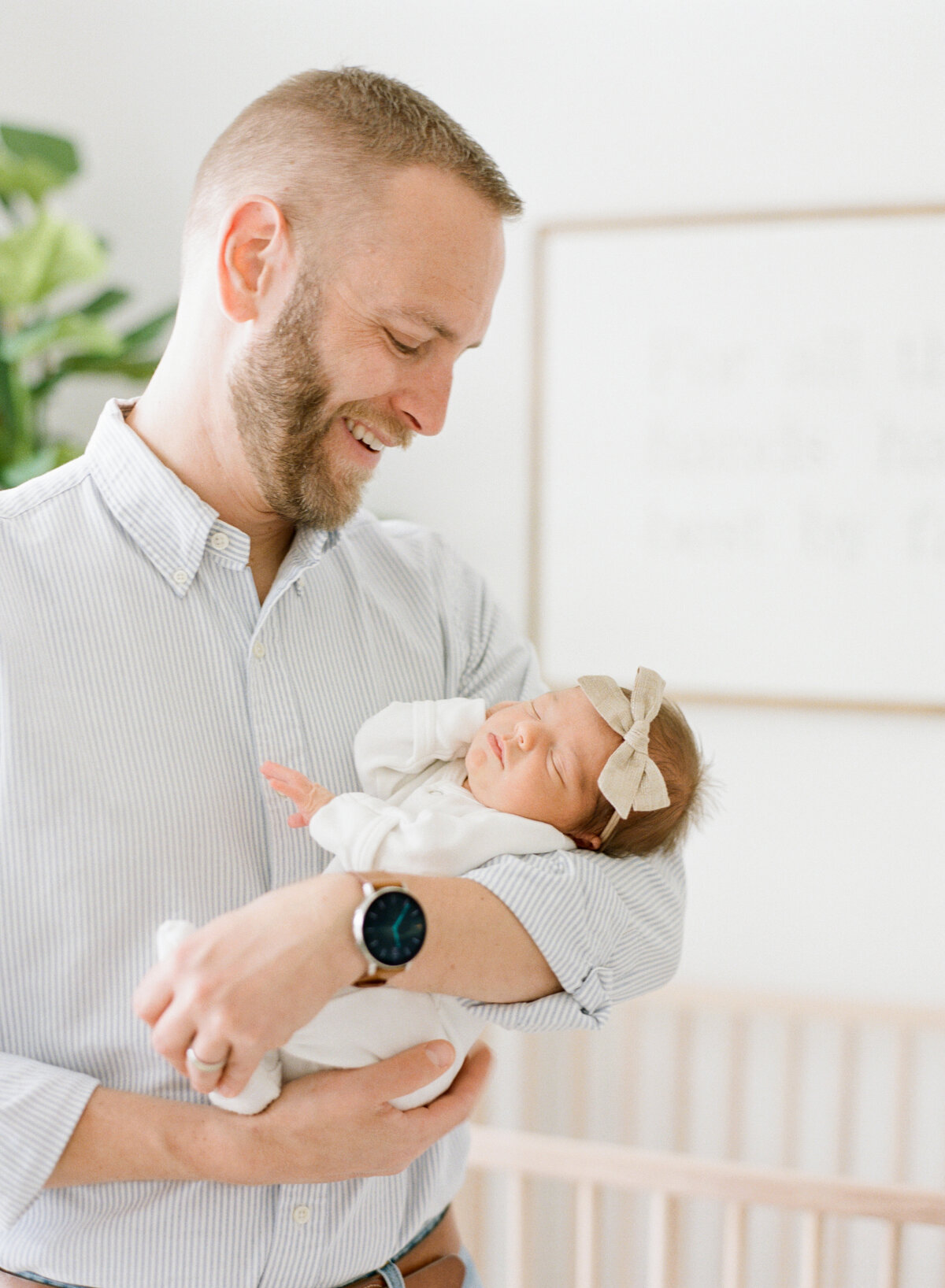 Dad holds baby in all white nursery while smiling at her lovingly during a Raleigh newborn photography session. Photographed by newborn photographer Raleigh A.J. Dunlap Photography.