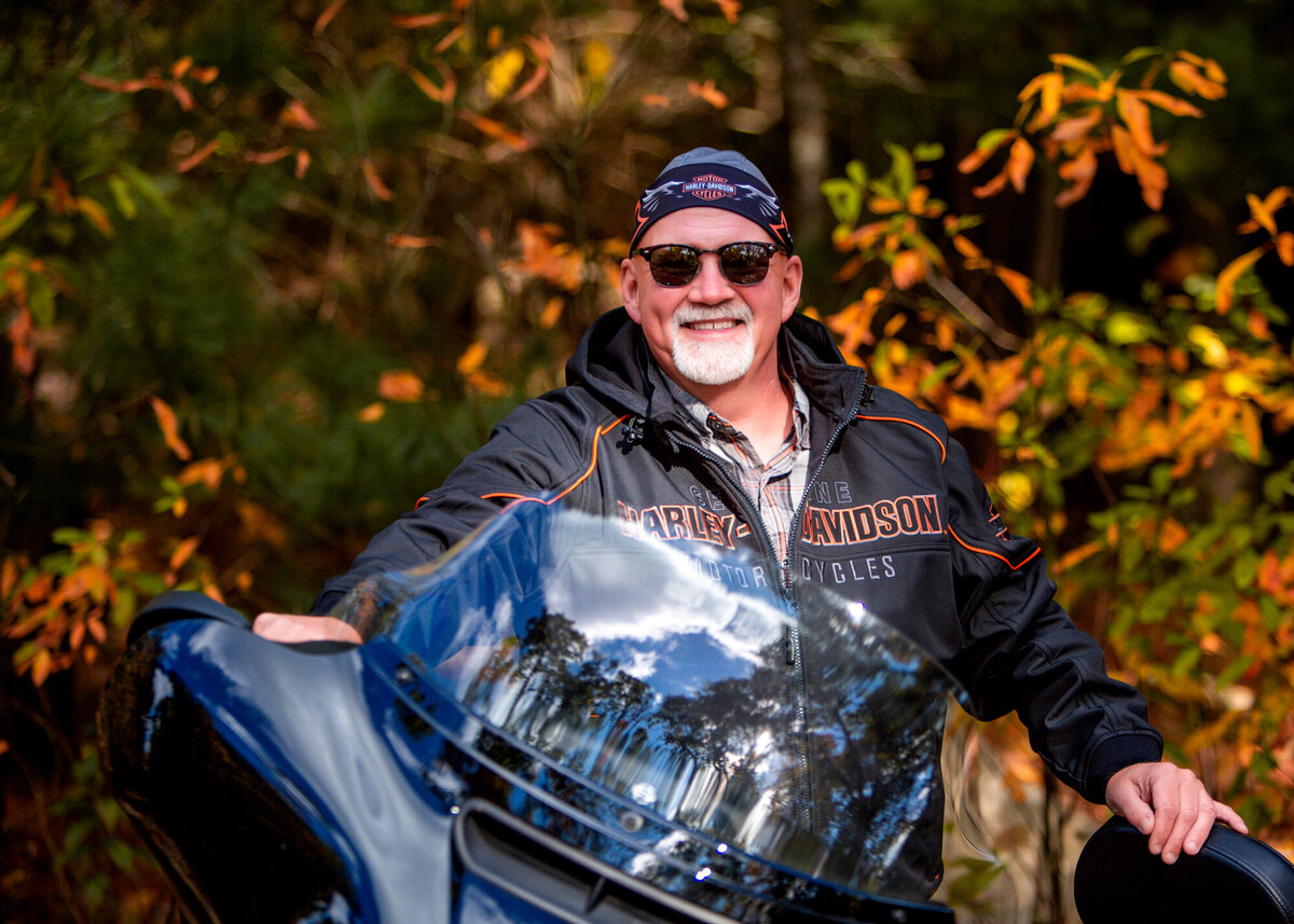 A male dating profile client standing behind his Harley Davidson motorcycle, wearing a leather jacket & do-rag, posing for a South Shore MA Portrait Photographer.
