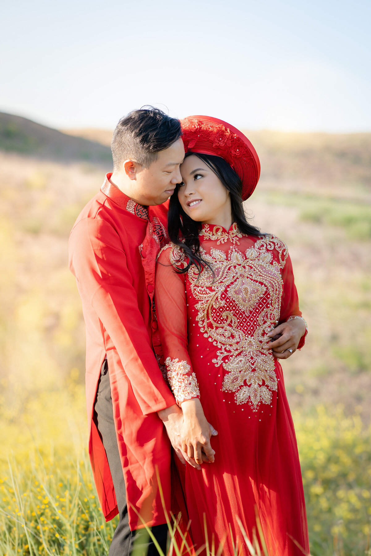 Couples portrait of Asian bride and groom eloping at Malibu Sate Park wearing Vietnamese red Ao Dai red within golden wildflower field and mountains