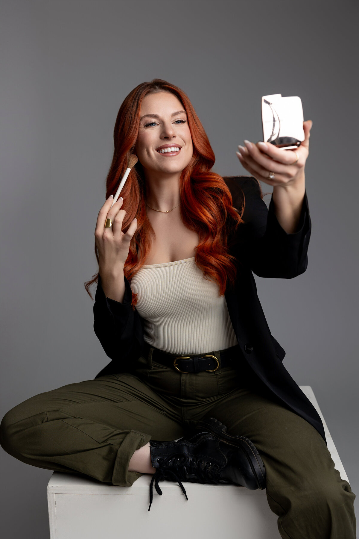 Red-haired woman adjusting makeup products while seated in studio. Photograph by Yucaipa branding photographer Kaitlyn Dawn Photography.