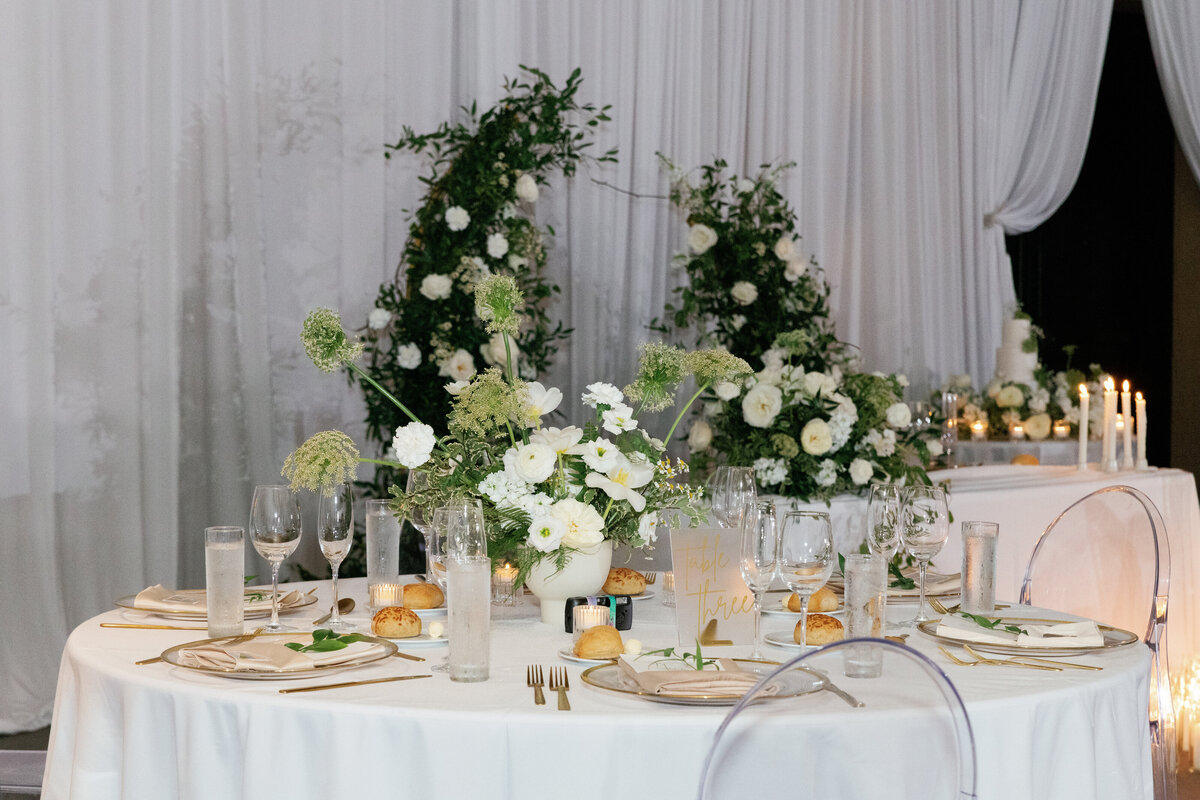 ghost chairs around table with white tablecloth with whimsical green queen annes lace and white poppy centerpiece with bread and water