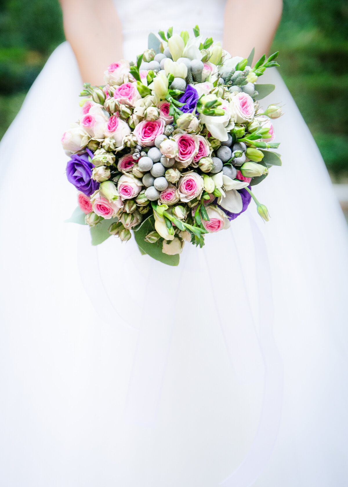 A bride in a white dress holds her colourful bouquet towards the camera.