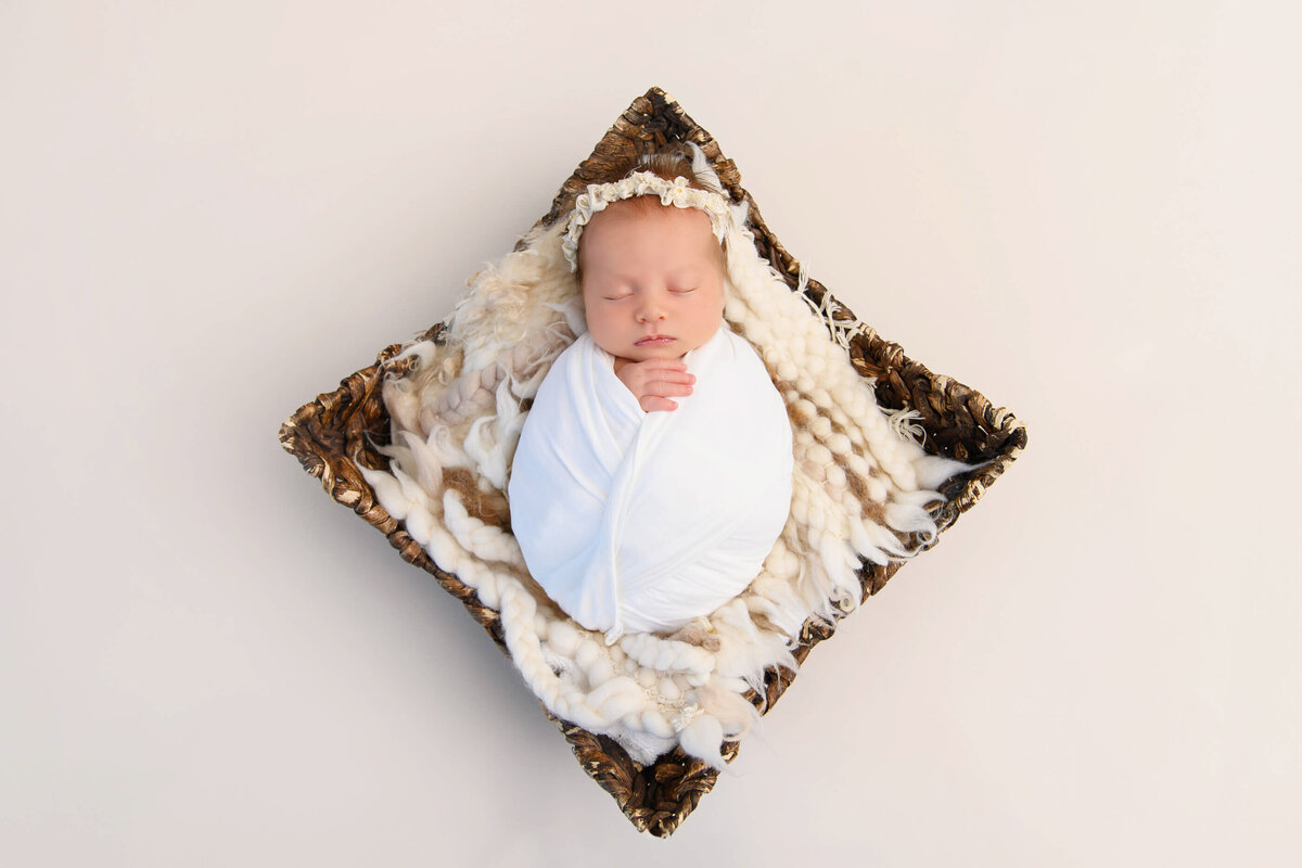 newborn baby girl wrapped in white in a basket for her newborn photos in Burlington, On