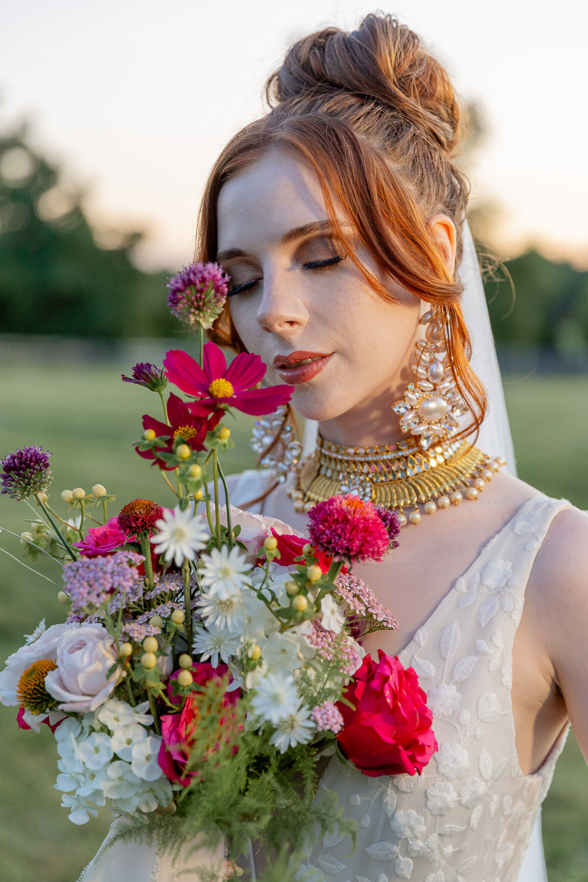 A bride holds a bouquet of bright pink flowers close to her face as she closes her eyes and smells the flowers.
