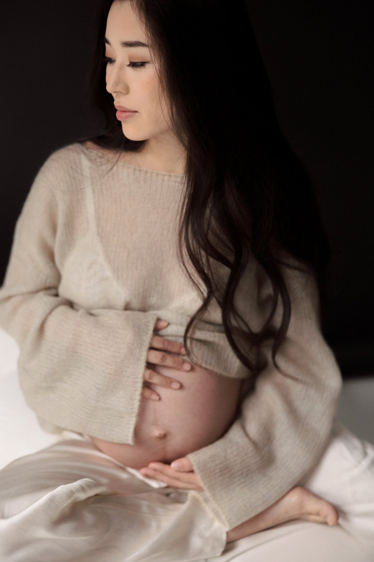 Pregnant woman holds belly as she poses in Brooklyn portrait studio.