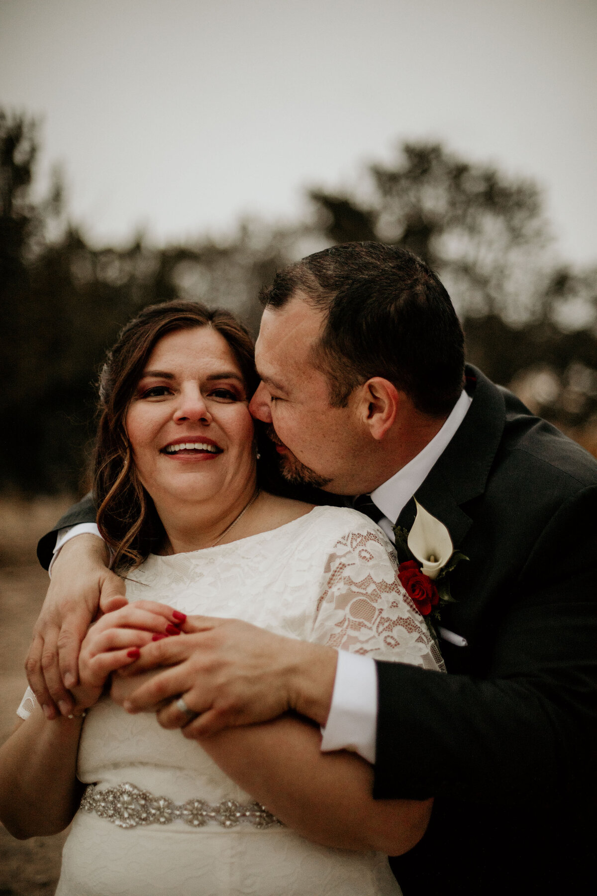 groom holding bride from behind whispering to her