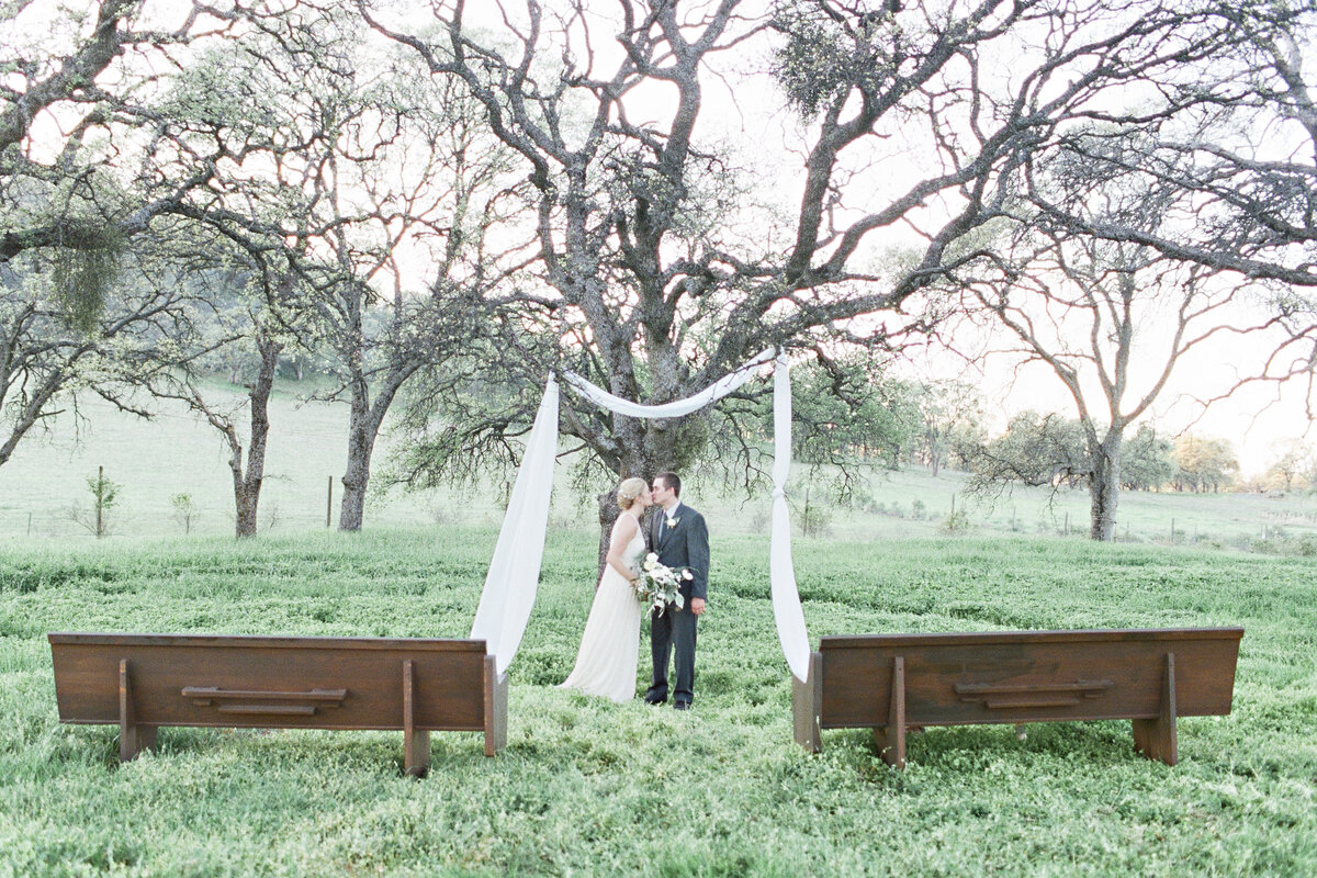 Bride and groom kissing under the trees at River Highlands Ranch