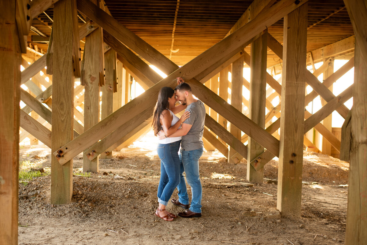 Capture the romantic moments of a couple's engagement photo under the pier at Galveston Beach, where their love is sheltered by the timeless beauty of the sea.