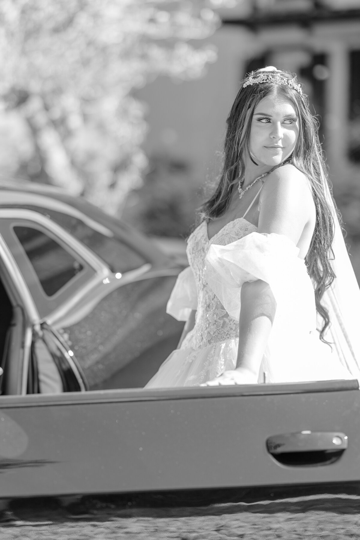 Black and white photo of a bride standing next to a Dodge charger before getting in