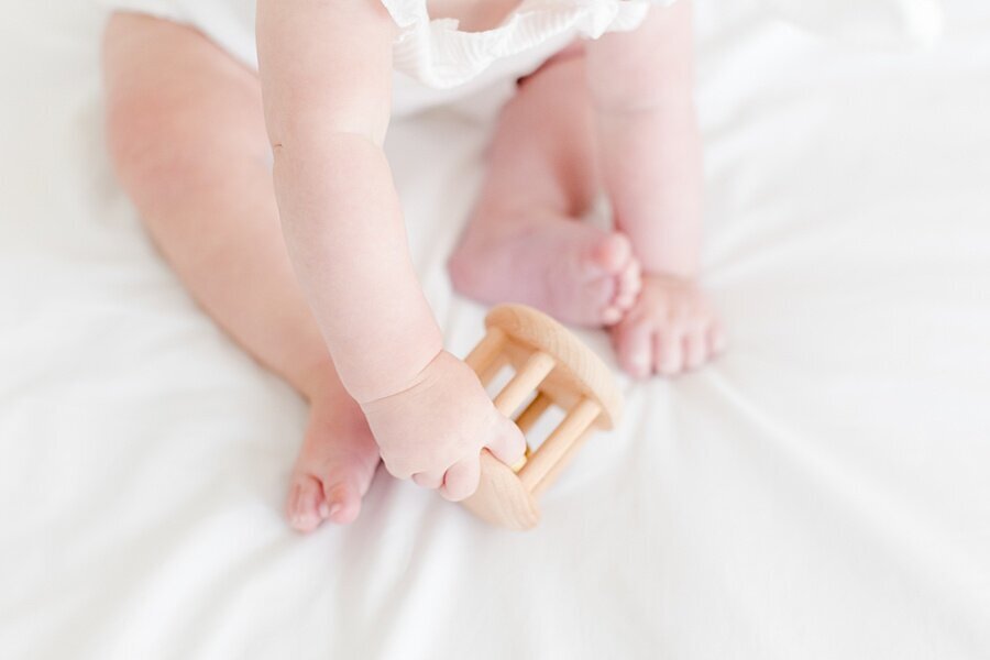 Detail shot of baby feet and hands playing with toy by milestone photographer Emily Gerald