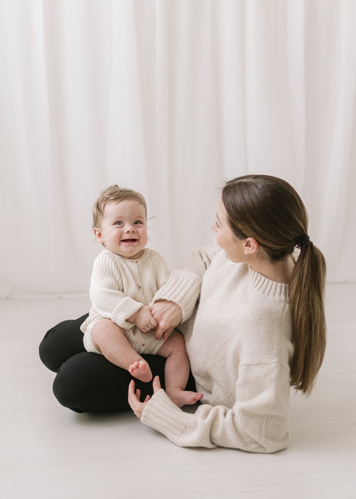 Mother sits with happy older baby during in a photo studio