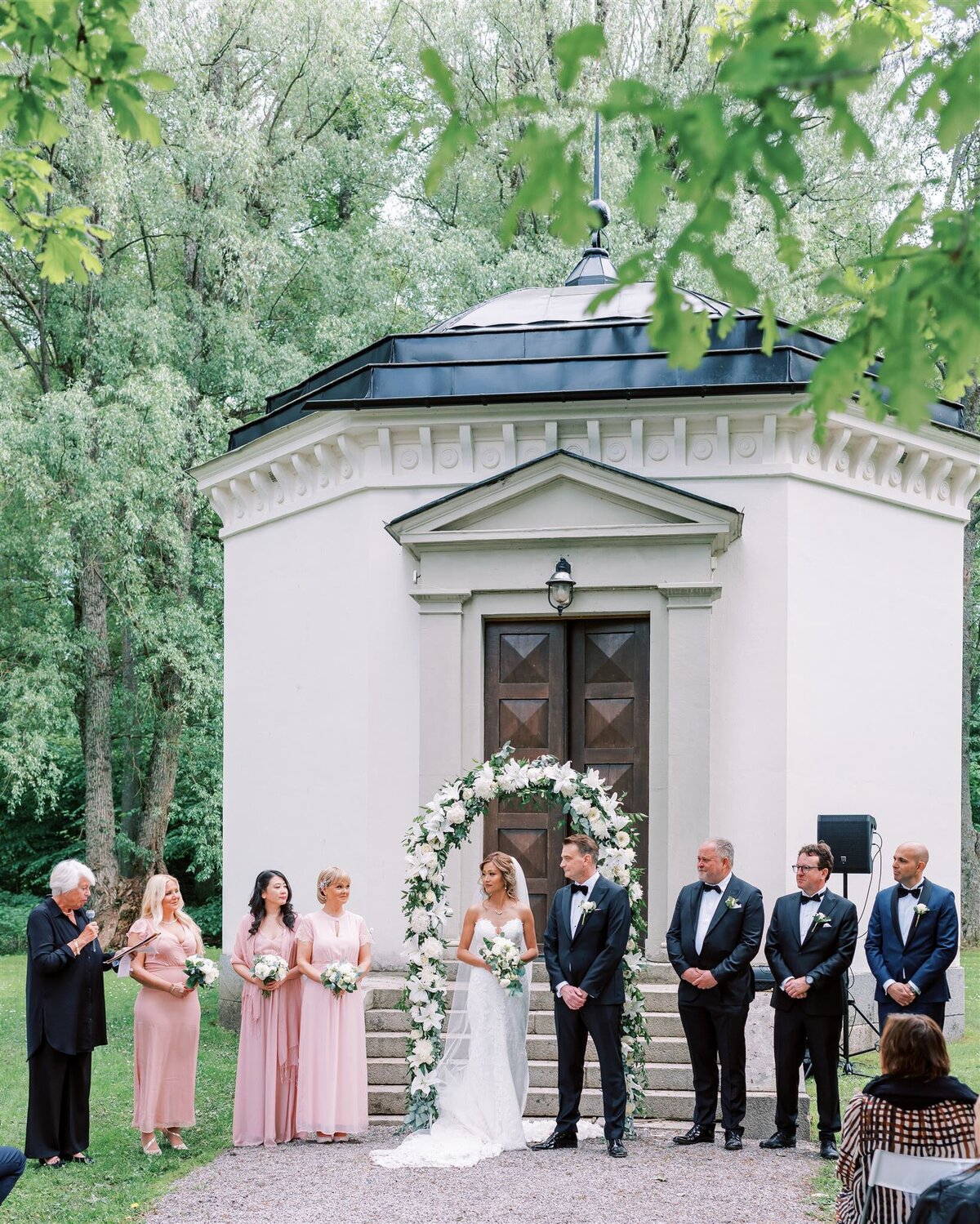 Destination Wedding Photographer Anna Lundgren - helloalora Rånäs Slott chateau wedding in Sweden outdoor ceremony with flower wedding arch wedding party and guests wedding smoking wedding officiant