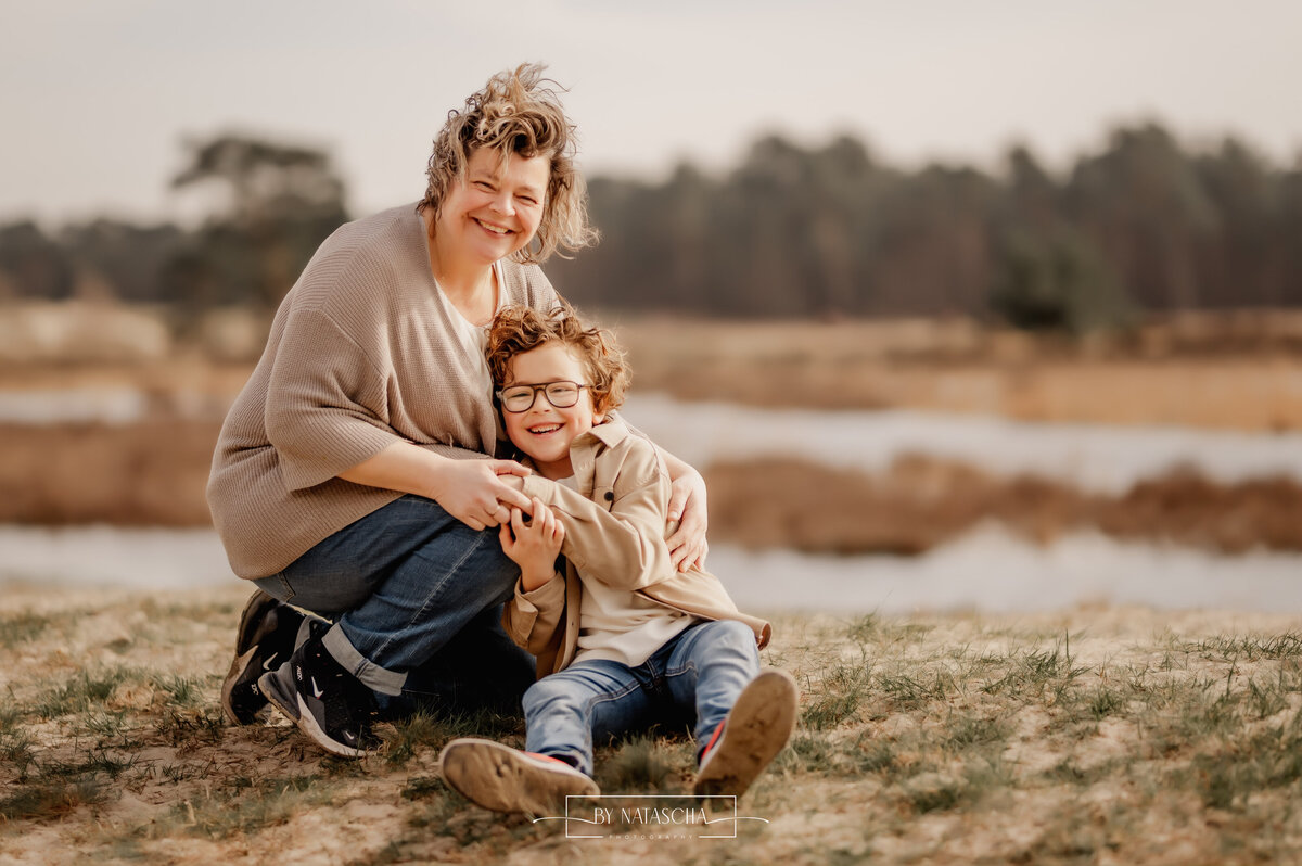 Mama en zoon zitten tegen elkaar aan en omhelsen elkaar bij de Drunense Duinen