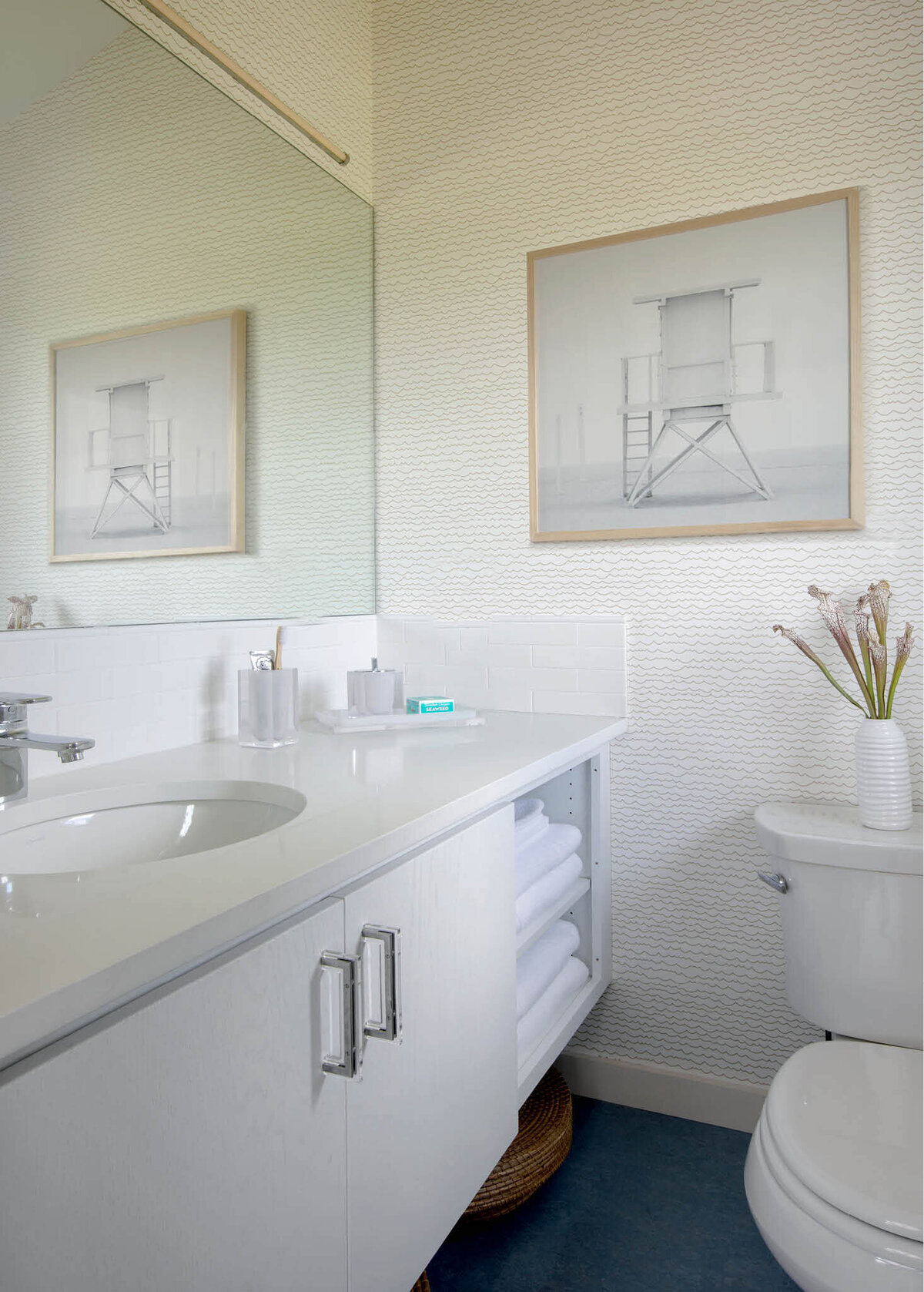 Martha’s Vineyard interior designer creates a simple bathroom with a white vanity, Schumacher wallpaper, modern lighting, and coastal art in a Cape Cod home renovation.