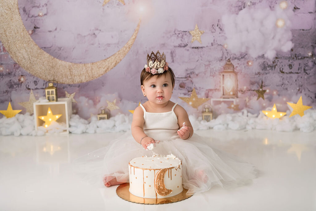 Portrait Photographers CT capture baby girl in ivory tulle dress with golden moon decorated cake at celestial themed first birthday cake smash